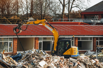 Construction equipment demolishing a brick building at a construction site during the day with...