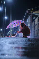 Little girl holding umbrella over stray kitten on street on rainy night