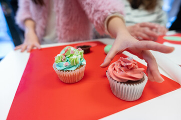 Young girl decorating cupcakes during a baking class preparing muffins and cupcake for birthday...