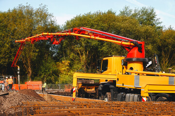 Construction crew using concrete pump truck during daytime on a construction site surrounded by...