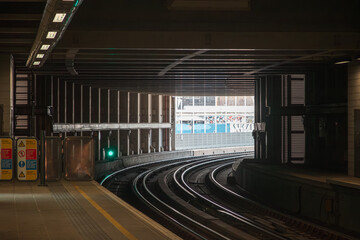 A dimly lit overground train station in London with curved tracks leading towards an opening