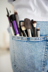 makeup brushes sticking out of blue jeans pocket on colorful white background. professional makeup...