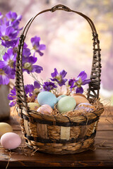Easter eggs in a basket and purple daisies with vibrant spring background