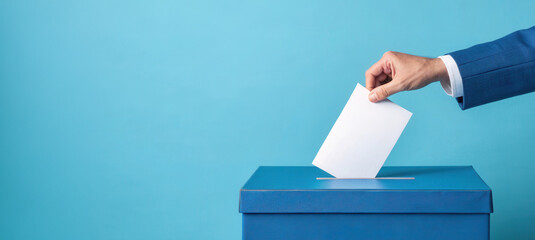 A hand is placing a ballot into a blue voting box against a light blue background, symbolizing the democratic process of voting.