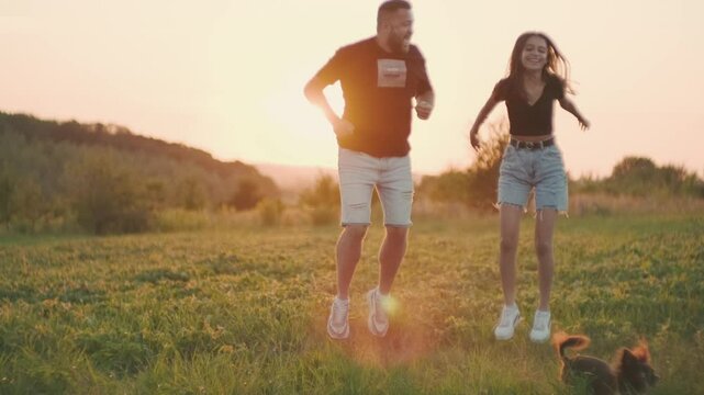 A boy and a girl are playing at sunset, jumping, having fun.Сouple is playing with a kind black domestic dog in the forest, on a  summer day.A happy family plays together in the park