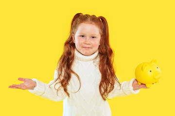 Little girl with red hair showing a piggy bank against a bright yellow background
