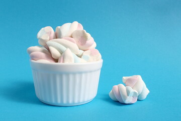 A white cup stands on a blue background with marshmallows.	