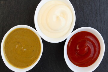 Three cups of salad dressing sit on a black stone board.