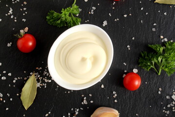 A white bowl of mayonnaise stands on a black background.	