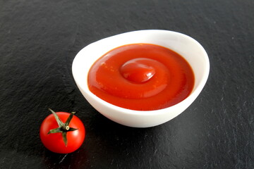 There is a white bowl with tomato sauce on a black isolated stone background.