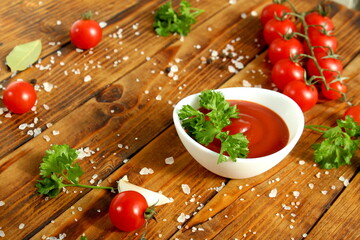 There is a white cup with tomato sauce and tomatoes on the wooden table.