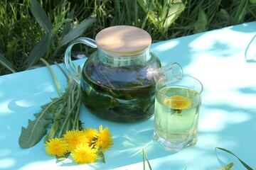 There is a glass teapot with dandelion tea on a wooden table.	
