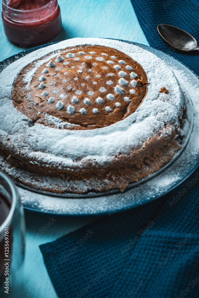 Sticker Homemade cake sprinkled with powdered sugar on a light blue background with a blue napkin and a cup of tea on the table.