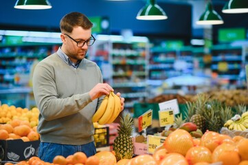 Handsome man with shopping trolley in fruit and vegetable department of supermarket
