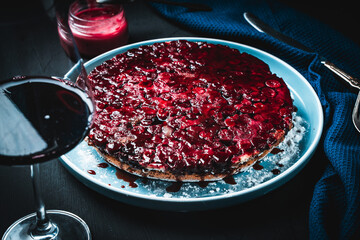 Delicious cherry clafoutis or French berry pie and a glass of red wine on a black background with a blue napkin.