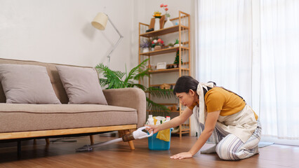 Obraz premium Asian housemaid vacuuming the wooden floor in a cozy living room with cleaning equipment