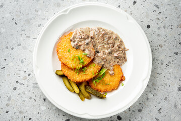 A plate of crispy potato pancakes served with a creamy gravy and garnished with fresh herbs, accompanied by pickles. Perfect for showcasing comfort food in a cozy dining setting.