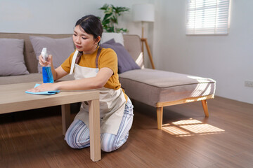 Close-up of an Asian housemaid cleaning a wooden table with a spray bottle and microfiber cloth