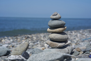 Balancing rocks on a pebble beach during sunset. Smooth pebbles on the beach against the background of the sea and sunlight, creating a side effect on the water. High quality photo