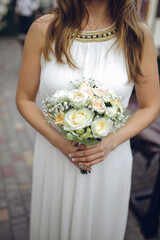 A bride in a white gown with beaded neckline holds a delicate bouquet of white and peach roses...