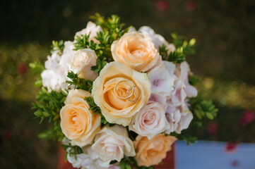 A close-up of a wedding bouquet featuring peach and cream roses, greenery, and a pair of wedding rings nestled inside a bloom.  
