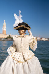 Back view of a woman in an elegant ivory Venetian carnival gown and feathered hat, gazing at...