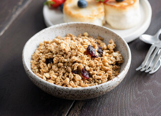 Crunchy granola with dried cranberries in a bowl, closeup view, wooden table background