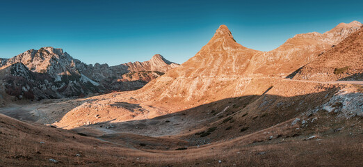 Golden hour sunlight bathes Sedlo pass in Durmitor national park, Montenegro, highlighting the rugged mountain peaks and creating a dramatic landscape