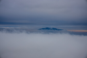 Winter cloudscape mountains view. Fog and mist on the sky with some dark clouds in a freezing morning air among the mountains and hills in Brasov, Romania