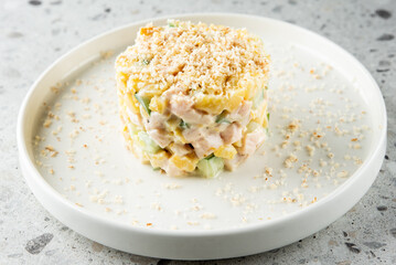 A beautifully layered salad on a white plate, featuring diced vegetables and chicken, topped with a crunchy layer of breadcrumbs. The dish is garnished elegantly, showcasing fresh ingredients.
