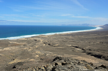 Endless lonely sand beach, playa Cofete, volcanic hills in the background  roaring atlantic and lava streams. Fuerteventura, Canary Islands, Spain