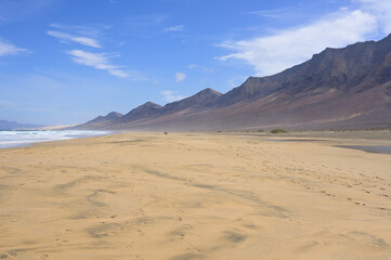 Landscape panorama of the endless lonely nature sand beach of playa Cofete, volcanic hills in the background and roaring atlantic. Fuerteventura, Canary Islands, Spain