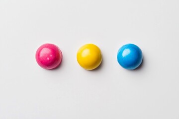 Colorful round candies in pink, yellow, and blue arranged on a clean white surface for a bright and cheerful display