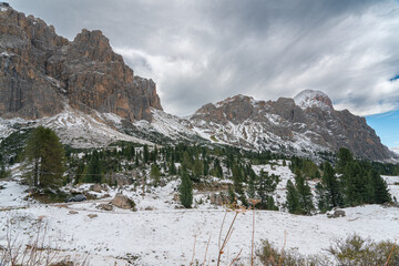 Snow-covered alpine meadows and towering mountains under a dynamic sky. A perfect scene showcasing the raw beauty of winter in the Dolomites.