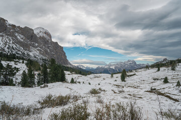 Snow-covered alpine meadows and towering mountains under a dynamic sky. A perfect scene showcasing the raw beauty of winter in the Dolomites.