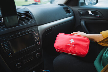 A person is currently seated inside a vehicle, actively holding and managing a first aid kit,...