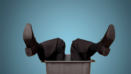 Businessman's legs in black trousers and shoes stuck upside down in a plastic trash can. The concept of "over the barrel". To be fired