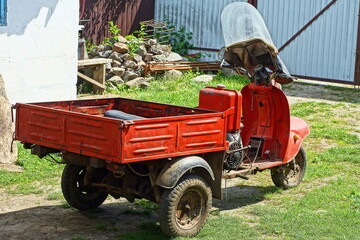 one power old retro iron red dirty heavy with three wheels and an empty trailer industrial scooter standing on the green grass during the day outdoors