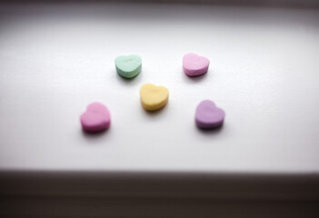 five pastel Valentine's Day hearts in pink, green, yellow, and purple against white wood in natural...