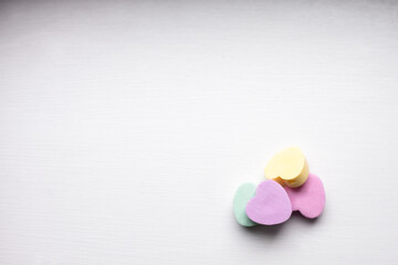 close-up of a pile of pastel candy hearts in pink, green, yellow and purple on w white wooden...
