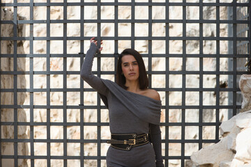 Young, beautiful woman dressed in gray leaning on her back and holding on to the gray metal grille....