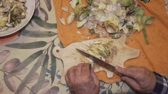 zenithal image of an old man's hands chopping alcarchofa on a wooden board in the shape of a pig, colourful vegetable in a vegetarian meal.
