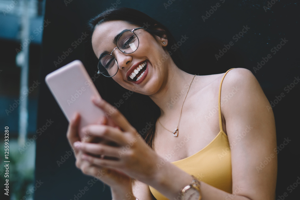 Poster cheerful millennial female blogger in eyewear checking mails and text messages via mobile technology