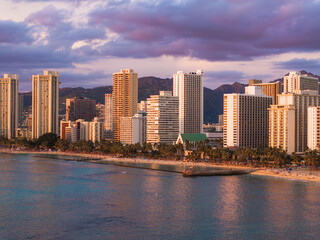 Obraz premium Waikiki Beach in Honolulu, Oahu, Hawaii, at sunset with calm ocean waters, palm lined shore, high rise buildings, and distant mountainous terrain.