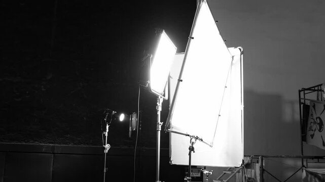 Video production studio lighting setup with diffuser softbox continuous lights and equipment stands against a dark backdrop. Ideal for photography filmmaking and commercial video production footage.