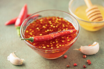 Hot honey in bowl and  chili peppers on green background.