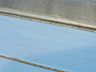 The light blue ship wall of a fishing boat with galvanized, riveted steel and railing looks...