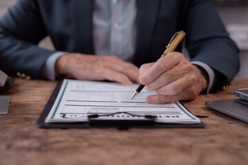 Fototapeta premium Close-up view of businessman hands diligently filling out an application form with a pen on a wooden desk, surrounded by documents related to contracts and investment agreements