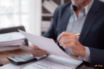 Close-up of hands of senior businessman holding and reviewing documents with pen, preparing to sign contract in office, concept of business, finance, and accounting