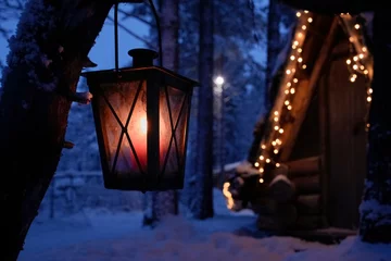 Fototapeten Cozy lantern glowing near a cabin adorned with Christmas lights during a serene polar night in Lapland on Christmas Eve. festive charm and peaceful magic of a winter holiday season © Oleksandr Bochkala